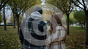 Back view of loving couple walking in autumn park in daytime. Romantic lovers .