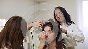 Back view of makeup artist make up eyebrow of young woman with brush in beauty salon. Professional hairdresser making