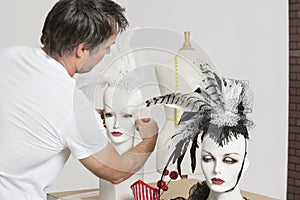Back view of male fashion designer adjusting feather fascinator on mannequin