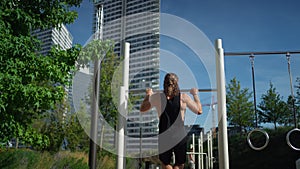 Back view of male sportsman doing pull ups on the horizontal bar while training outdoors