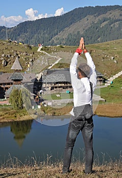 Back view of a male tourist making namaste gesture while standing towards Parashar rishi temple in Mandi, Himachal Pradesh, India