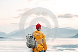 Back view of male tourist with rucksack standing on coast in front of great mountain while journey