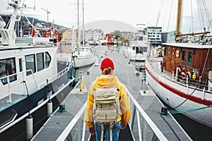 Back view of male tourist with traveling backpack wearing yellow raincoat standing on pier