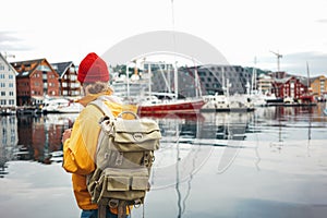 Back view of male tourist with traveling backpack wearing yellow raincoat standing on pier