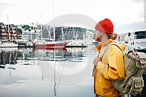 Back view of male tourist with traveling rucksack standing among fishing boat on city pier