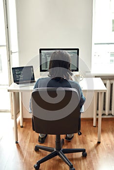 Back view of male web developer writing code while sitting at his workplace and working from home, writing code. Using photo