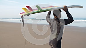 Back view of man with disability carrying surfboard on head