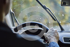 Back view of a man driving a car with moving windshield wipers during rain