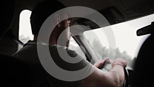 A back view of a man driving a car in the rain. Hands on a steering wheel, wipers working.