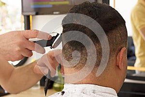 Back view of man getting short hair trimming at barber shop with clipper machine