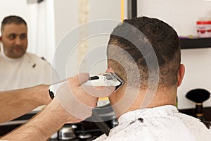 Back view of man getting short hair trimming at barber shop with clipper machine