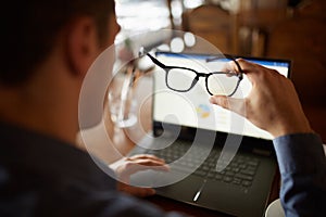 Back view of man hand holding eyeglasses in front of laptop screen with charts and diagrams. Poor eyesight threatment photo