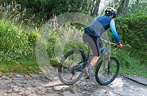 Back view of a man with a helmet riding a mountain bike on a forest trail