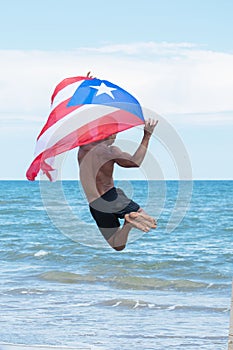 Back view of a man holding a cuban flag while jumping on the beach.