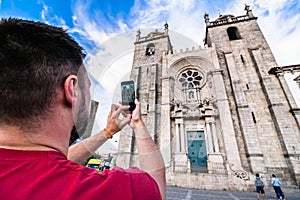 Back view of man, making shot of facade of cathedral in Porto. Tourist with beard taking a photo of Porto Cathedral or Se Catedral