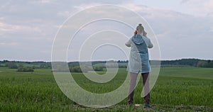 Back view of man observing something in binoculars standing on green field landscape. Unrecognizable traveler looking