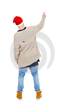 Back view of a man in a Santa Claus hat pointing upwards.