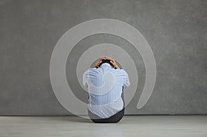 Back view of man sitting on floor, holding head, feeling distressed, frustrated and hopeless