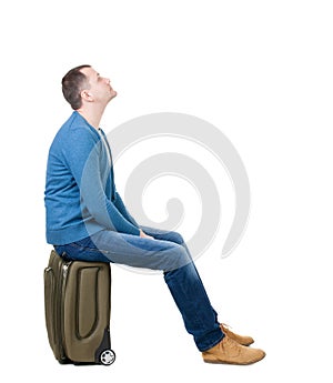 Back view of a man sitting on a suitcase.