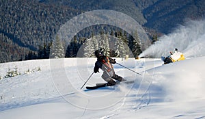 Man skiing on prepared slope with fresh snow. Snow gun machine making artificial snowfall. Magic nature on background.