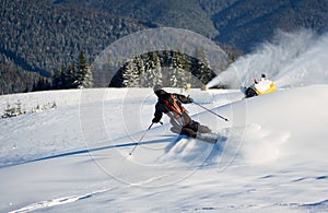 Man skiing on prepared slope with fresh snow. Snow gun machine making artificial snowfall. Magic nature on background.