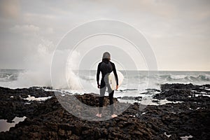 Back view man standing with a white surf in his hands on the beach