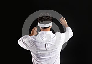 Back view of man touching invisible screen while experiencing cyberspace in vision pro VR glasses, black background