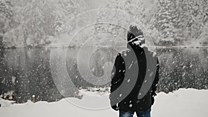 Back view of the man in warm winter clothes during the snowfall near lake Blausee in Swiss Alps. Steadicam tracking shot