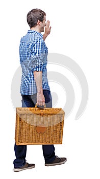 Back view of a man who comes with a suitcase for a picnic welcomes someone with his hand