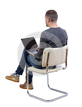 Back view of a man who sits on a chair with a laptop