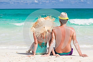 Back view of a man and woman couple sitting on caribbean white sand beach