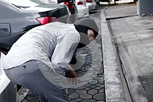 Back view of masked thief in black balaclava trying to break into car. Criminal crime concept.