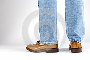Back View of Mens Legs in Brown Oxford Brogue Shoes. Posing in Blue Jeans Against White Background