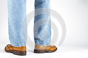 Back View of Mens Legs in Brown Oxford Brogue Shoes. Posing in Blue Jeans Against White Background