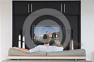 Back view of mid-adult man changing channels with television remote control in living room