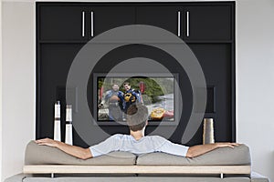 Back view of mid-adult man watching television in living room
