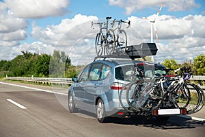 Back view modern white family wagon car with mounted roof box trunk and bike tail carrier driving european highway road