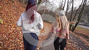 The back view of the morning jog of two attractive multicultural girlfriends. The park location.