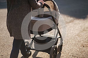 Back view of mother walking with her baby in stroller. Grey stroller outside, sunset