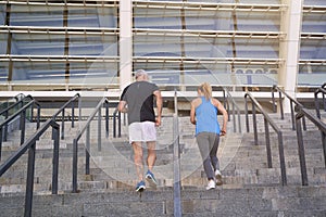 Back view of motivated couple, man and woman in sportswear running up a flight of stairs while training together