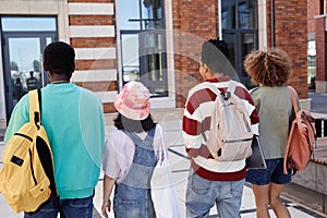 Back view of multiethnic group of young students walking in row outdoors