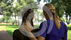 Back view of mum and daughter walking in park, conversation about life, advising