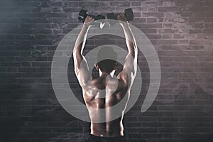 Back view of muscled man exercises with dumbbells