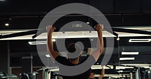 Back view muscular man doing wide grip pull ups on horizontal bar. Powerful athlete pumping arm muscles with chin ups in