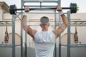 Back view of muscular man lifting barbells at public gym