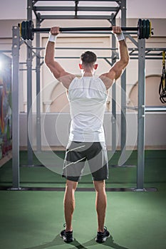 Back view of muscular man lifting barbells at public gym