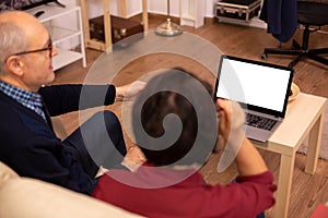 Back view of old couple in their living room looking a laptop with white isolated mock-up