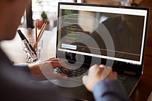 Back view over the shoulder shot of developer programmer with laptop. Program code and script data on the screen. Young