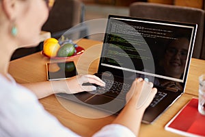 Back view over the shoulder shot of developer programmer with laptop. Program code and script data on the screen. Young
