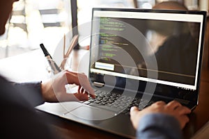 Back view over the shoulder shot of developer programmer with laptop. Program code and script data on the screen. Young